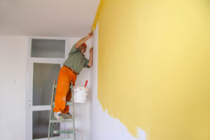 Painter In Action On A Ladder Painting Walls Yellow in Apartment Hiring Apartment Painting Contractors
