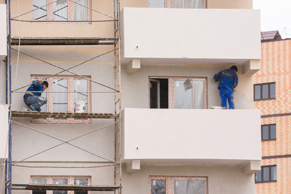 Two Painters Working On Exterior Repaint of Balconies And Walls At Apartment Building