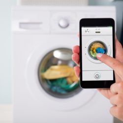 Person Using Laundry Room Mobile Apps On Smartphone To Control Washing Machine