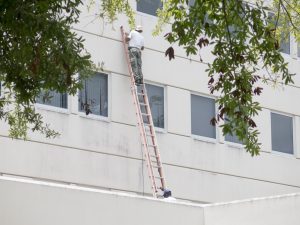 Worker On Ladder Performing Expensive Commercial Property Repairs