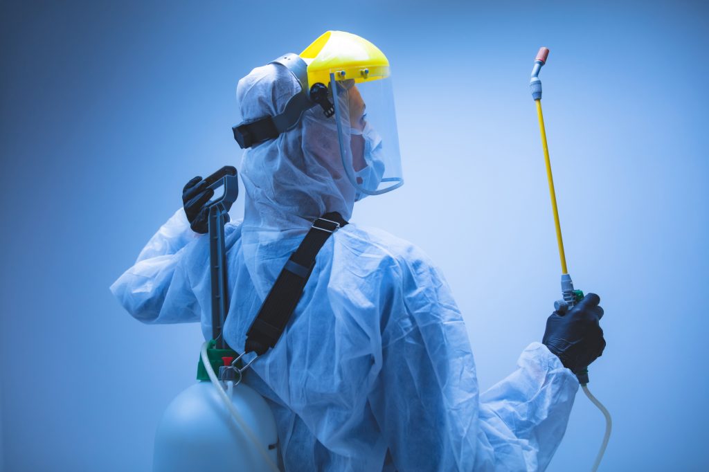 Commercial Cleaner In Hazmat Suit Disinfecting Commercial Office Buildings Against CoronaVirus With Chemical Sprayer