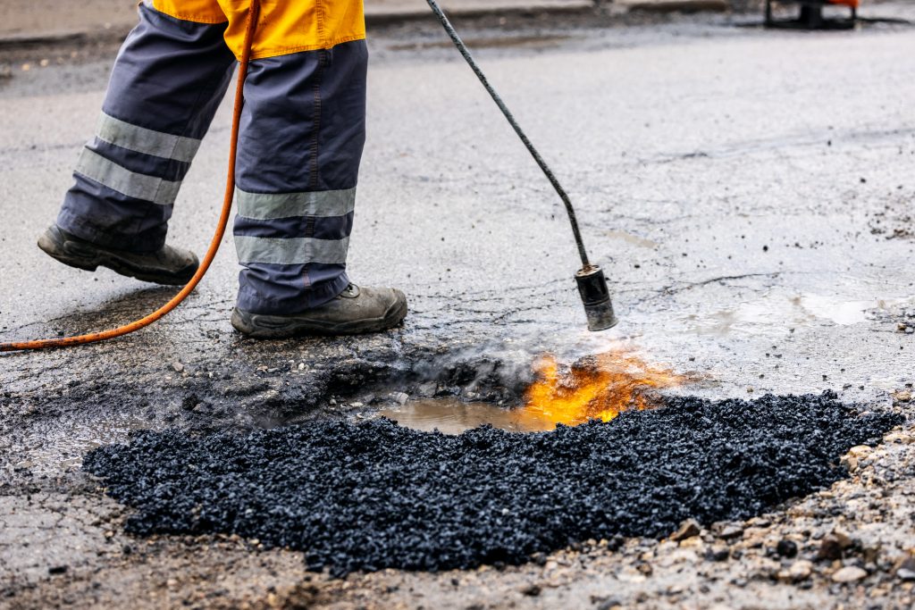 Worker Performing Commercial Pothole Repair Services Using Hot Mix Asphalt