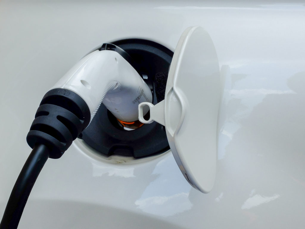 White Commercial Electric Vehicle Charging Plug Inserted Into Electric Vehicle