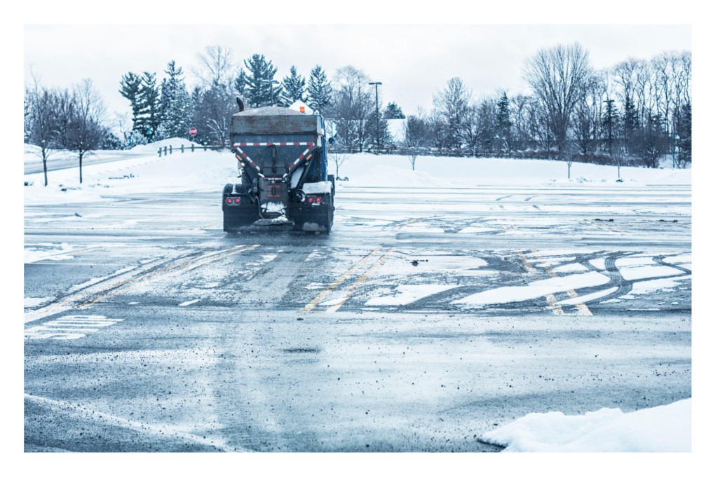 Snow Plow Spreading Salt In Essential Retail Store Parking Lot During Snow Event